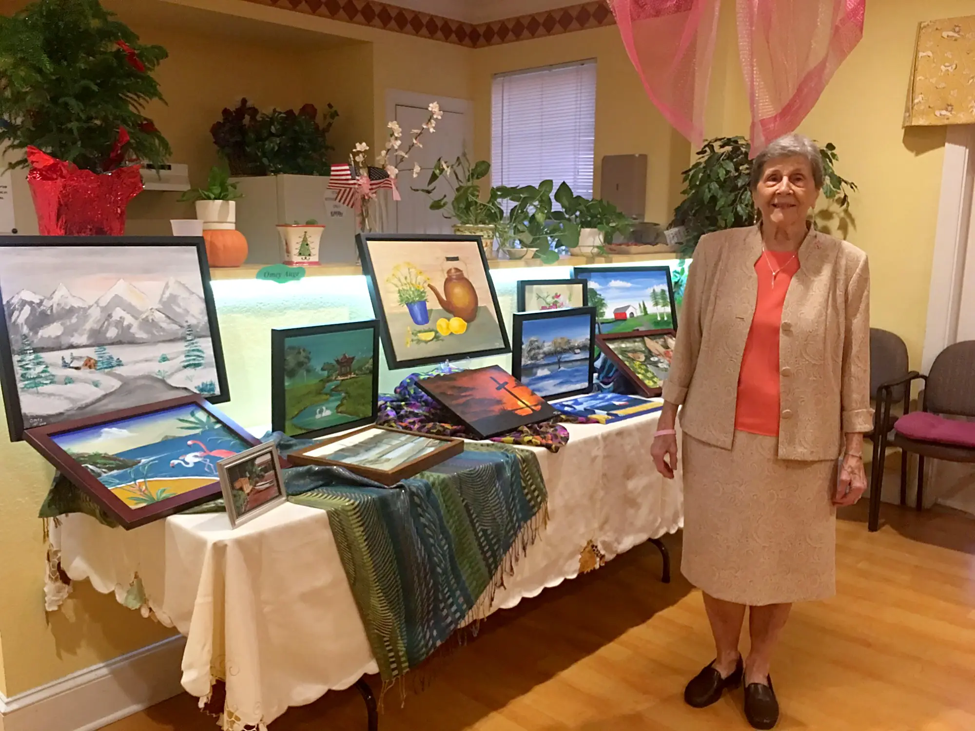 A senior artist beside a table of framed paintings at the class art show