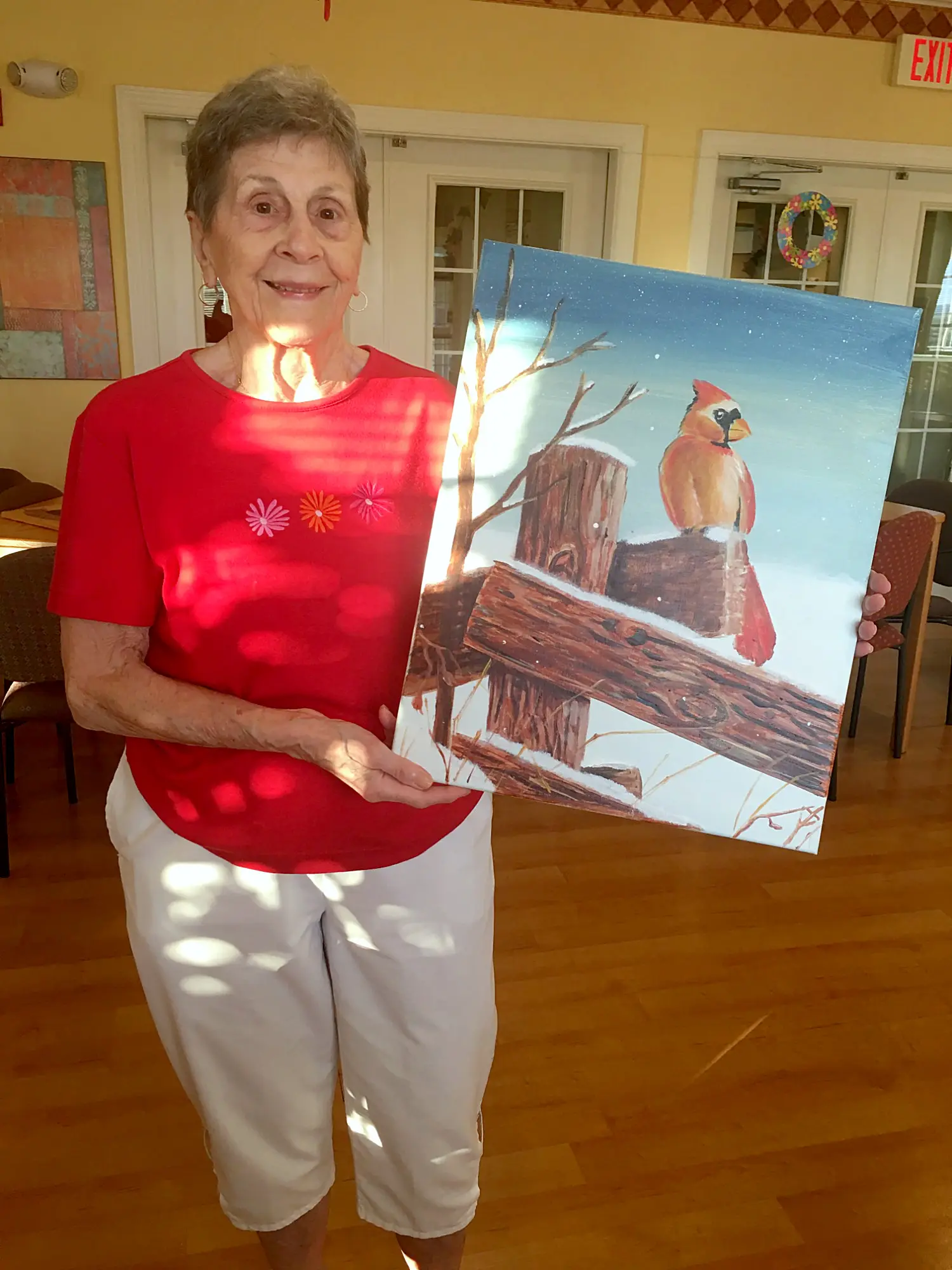 A senior artist holding a painting of a cardinal on a snowy fence